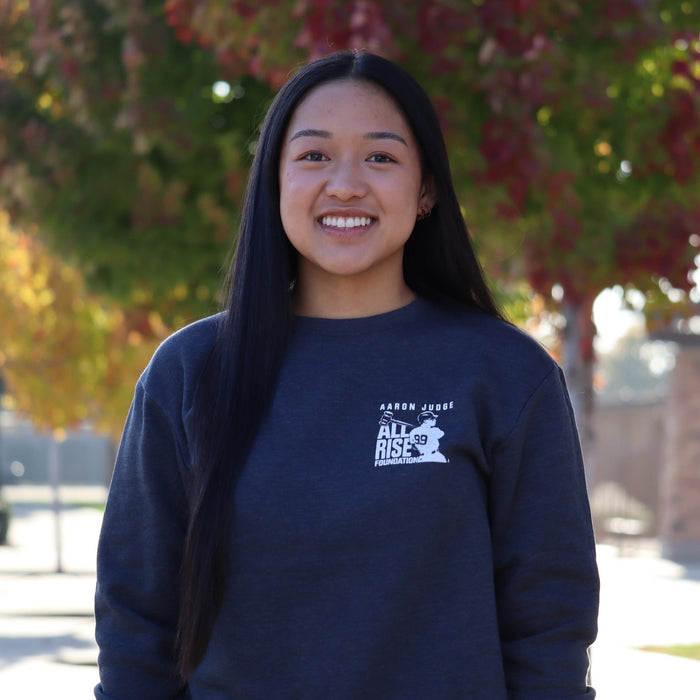 Young woman wearing our navy blue crew neck sweatshirt featuring the ALL RISE square logo on the left chest.