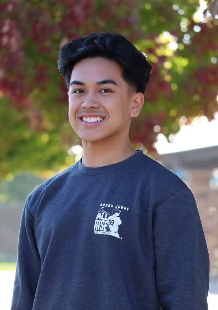 Young man wearing navy crew neck sweatshirt, featuring the square ALL RISE logo on the left chest.