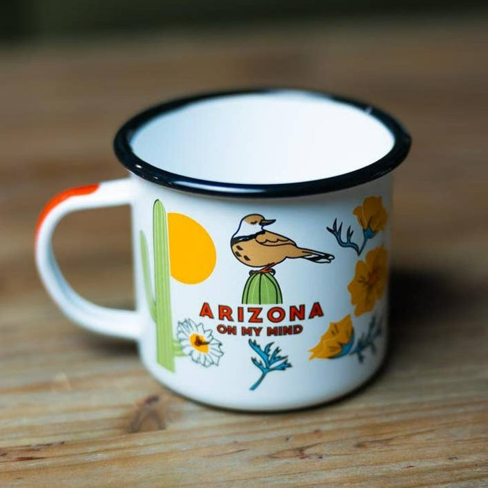 Enamel mug with a dark rim and orange handle featuring a desert scene and the words Arizona On My Mind.