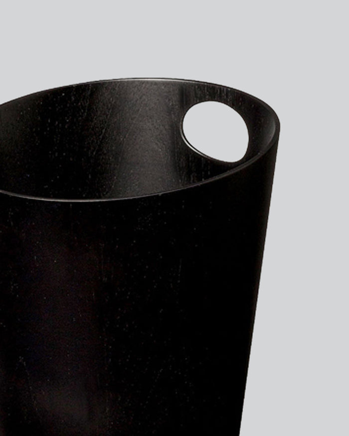 Cropped image focused on handle of black ash paper waste basket by Isamu Saito against white-gray background.