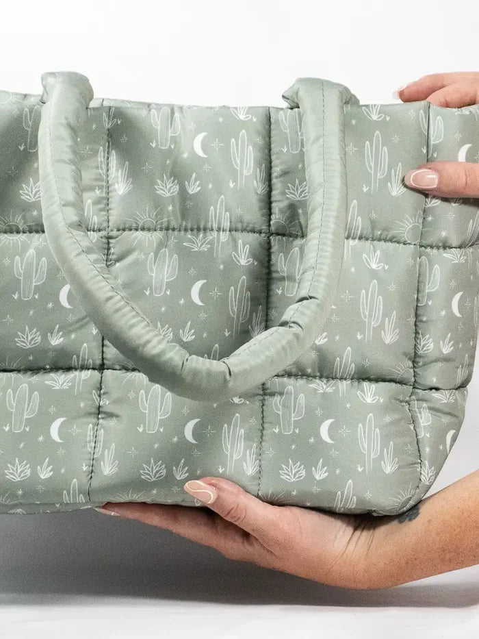 Cactus Cloud quilted puffer tote in sage green with cactus and moon print, held by hands.