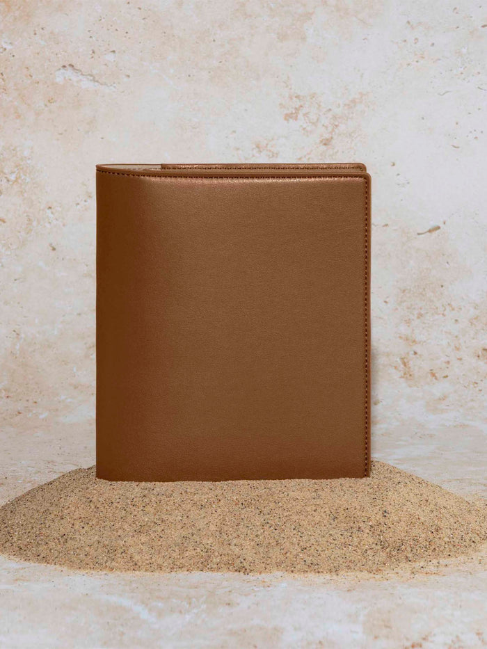 Folio displayed on a textured tan background, placed in a pile of sand. Color pictured is clay brown.