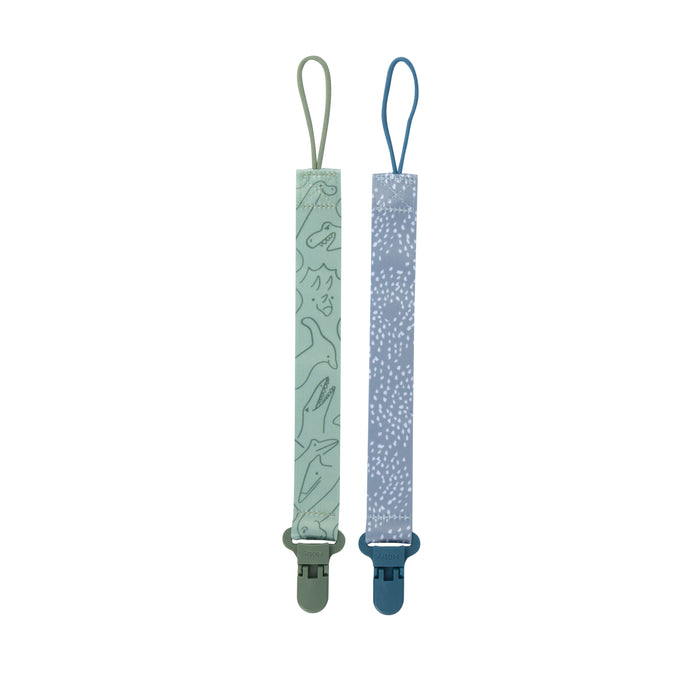 The Cloth Pacifier Clip (2 Pack) includes two fabric clips: one with a green dinosaur pattern and another in light blue with white dots, each featuring loops at the top and clips at the bottom, shown on a white background.