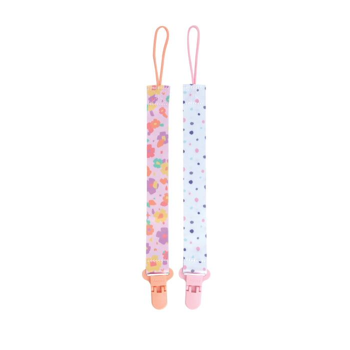 The Cloth Pacifier Clip (2 Pack) includes one with a pink and orange floral design with a peach clip, and another with multicolored dots on light blue with a pink clip—both featuring top loops to secure pacifiers.