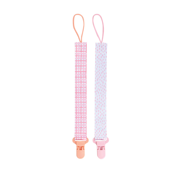 The Cloth Pacifier Clip (2 Pack) includes one pink checkered clip and one white clip with pink dots. Each baby pacifier holder features a top loop and a plastic bottom clip for easy, secure use.
