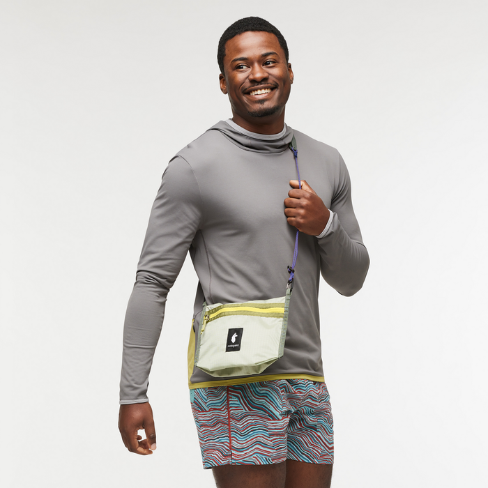 Man wearing a gray long sleeve top with a light green Lista 2L crossbody bag and a purple strap