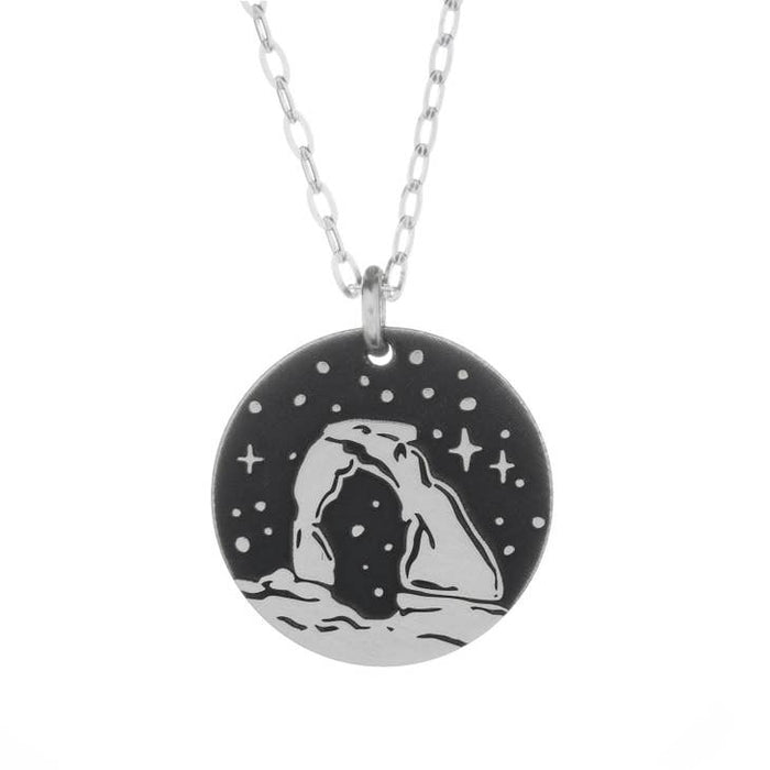 Round silver pendant necklace featuring a Delicate Arch silhouette against a starry night background.