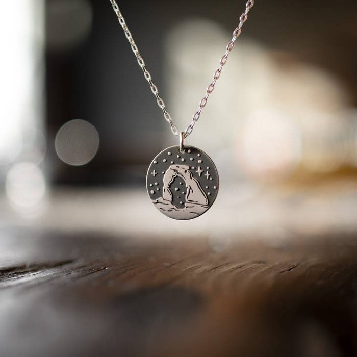 Close-up of the Delicate Arch round pendant on a silver chain with a soft, out-of-focus background.