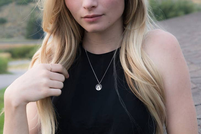 Model wearing the Delicate Arch round pendant necklace on a silver chain over a black top.