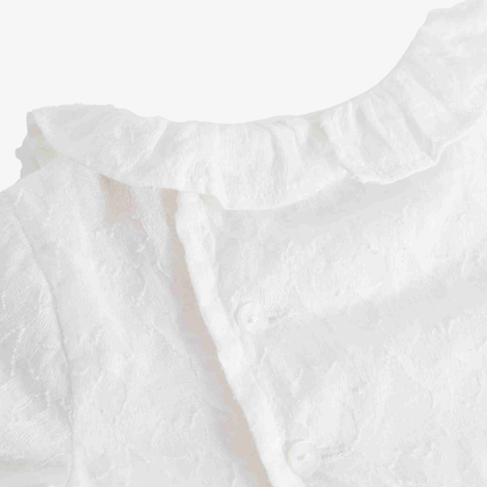 Close-up of a white textured baby top with a ruffled collar and button closure.
