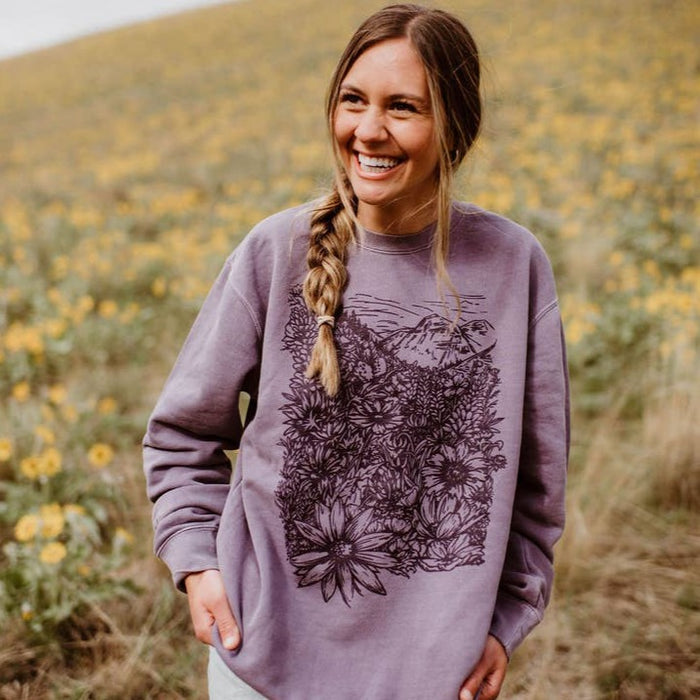 Woman wearing Flower Meadow Crewneck Pullover with bold floral graphic in a field of yellow wildflowers.