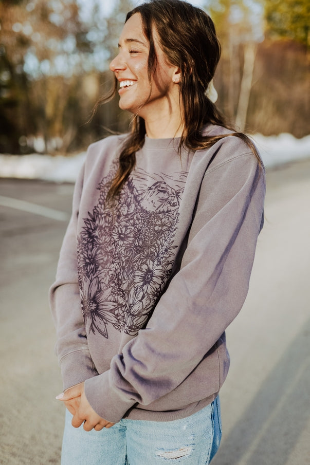 Side profile of a smiling woman wearing Flower Meadow Crewneck Pullover with a floral graphic.