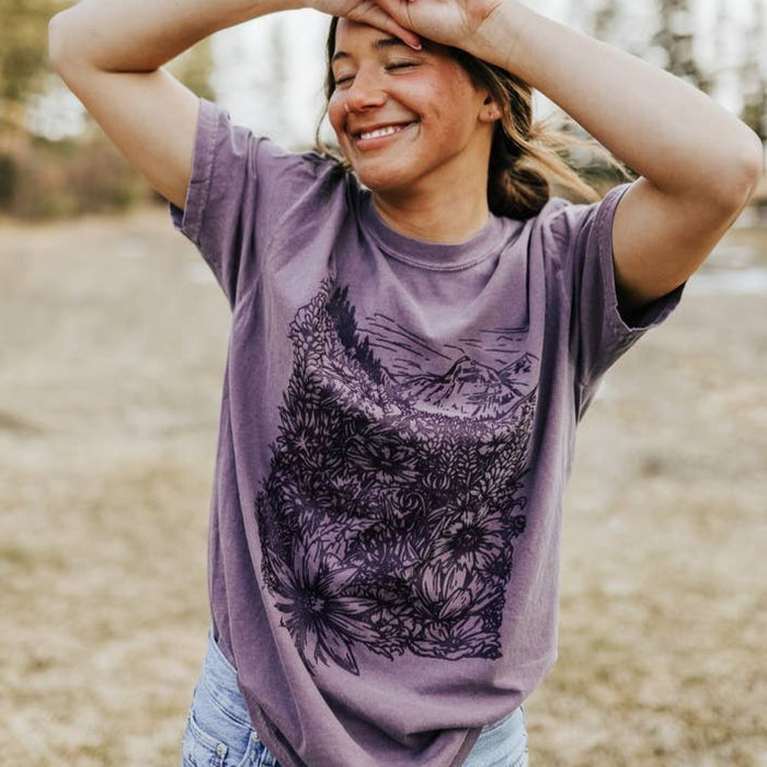 Woman outdoors wearing a purple Flower Meadow Tee with a bold floral graphic.