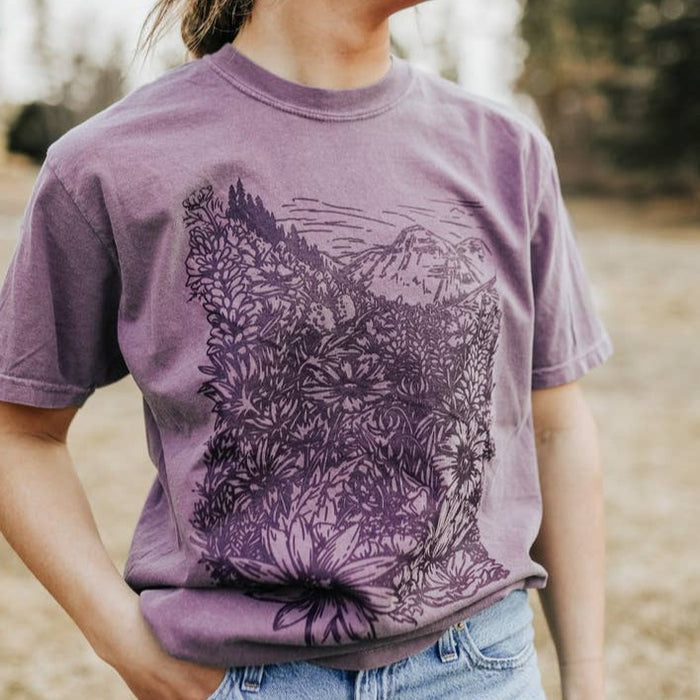 Close-up of a lavender Flower Meadow Tee showing a large floral landscape print.
