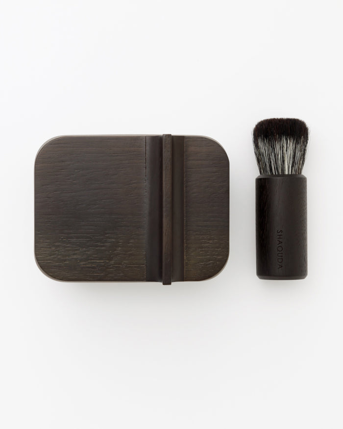 Image of hard Jiva face cleansing and shaving series with porcelain bowl next to  walnut, boar bristle, and goat hair brush by Shaquda against white-gray background.