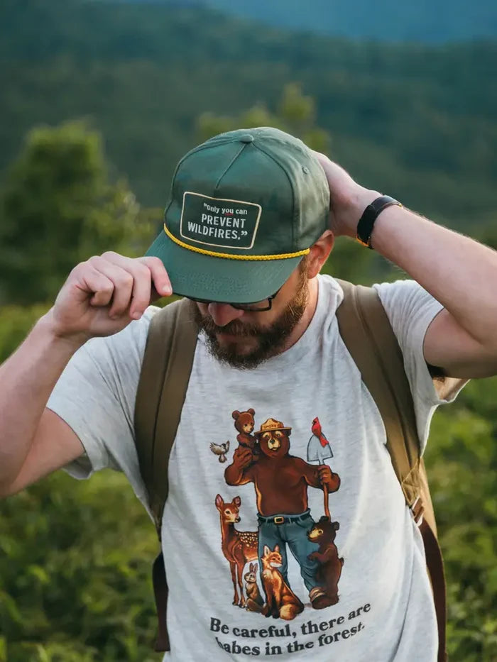 Forest green cap with yellow rope trim and a patch that reads only you can prevent wildfires worn by a hiker.