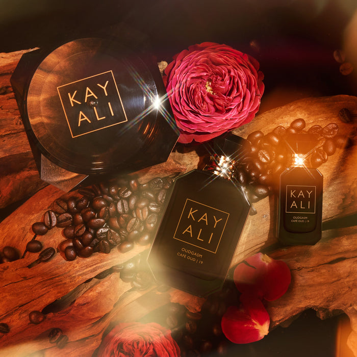 Two 'KAYALI' perfume bottles on a wooden surface with coffee beans and flowers.
