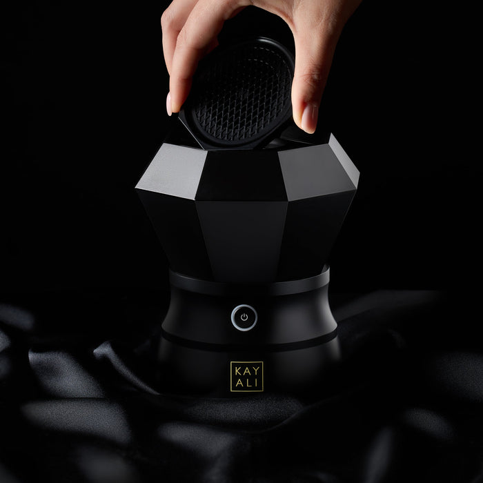 Black and white geometric bahkoor with a hand holding a black cap against a dark background, featuring the brand 'KAYALI'.