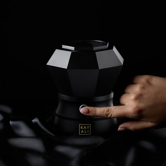 Black geometric device with a hand interacting with it on a dark background, featuring the brand 'KAYALI'.