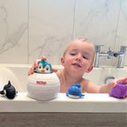 A young child enjoys bath time with the Penguin Pop-Up Bath Toy, shaped like an igloo, playing on the tub edge with included sea animal toys—a whale, dolphin, and purple creature—to enhance hand-eye coordination.