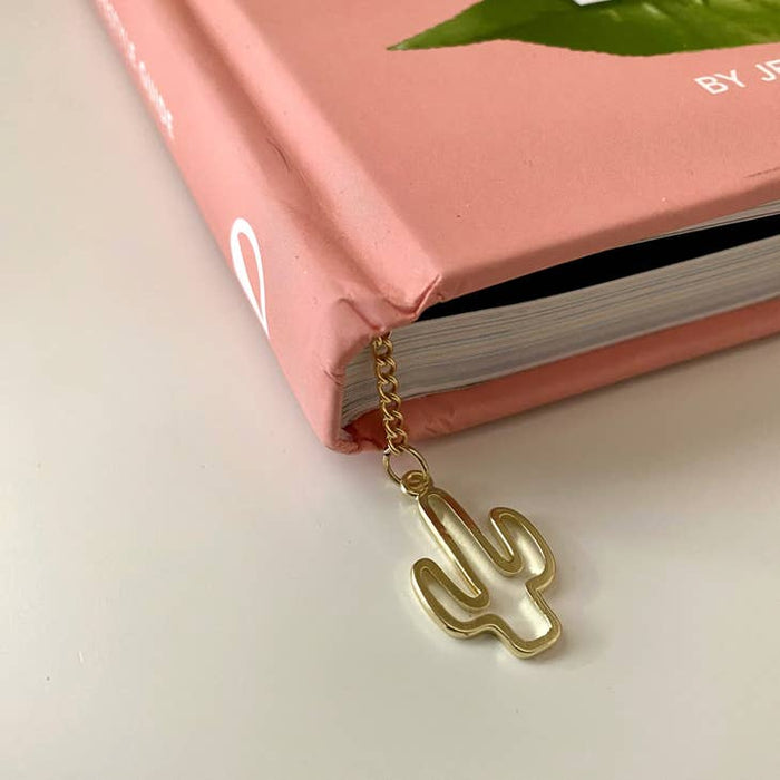 Gold cactus shaped bookmark on a delicate chain clipped to the corner of a pink book