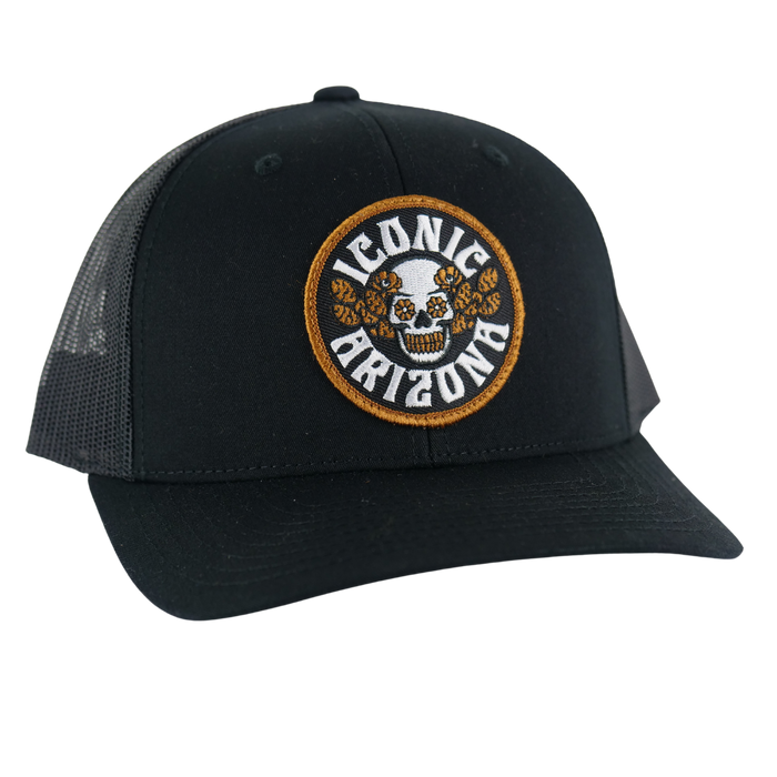 Black curved brim hat with round embroidered patch showing a skull surrounded by orange flowers and Iconic Arizona text.