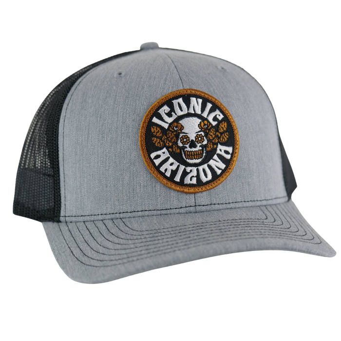 Gray curved-brim trucker hat with a circular embroidered patch showing a skull and orange desert roses