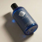 Upright studio product view of the cobalt blue 8.5 oz (255 ml) bottle of Sliquid Satin natural intimate moisturizer covered in fine water condensation, featuring a dark blue label and black cap.