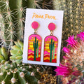 Stained glass Saguaro cactus earrings in pink orange sunset hues on a Paige Poppe card.