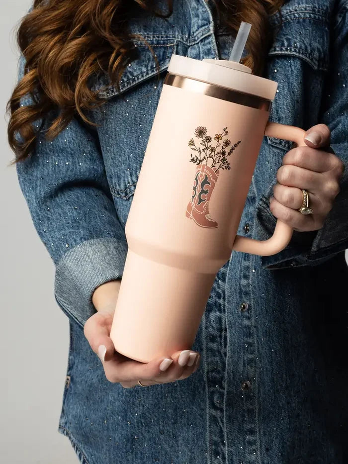 Peach insulated tumbler featuring a western boot and wildflowers, held by a person in a denim jacket