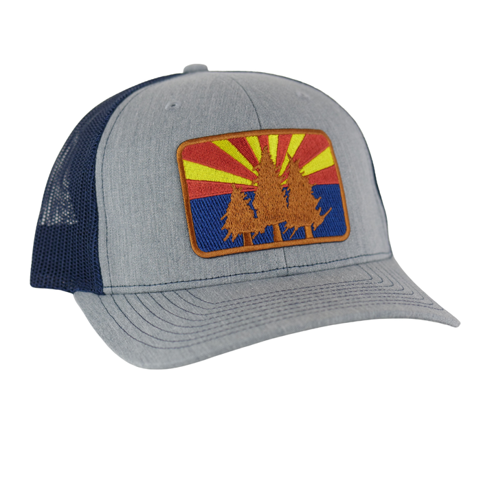 AZ Pines curved trucker hat with light gray front panel, navy mesh back, and a desert sunrise pine patch