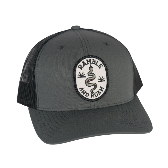 Grey curved brim trucker hat with a circular patch depicting a coiled snake and the words Ramble and Roam.
