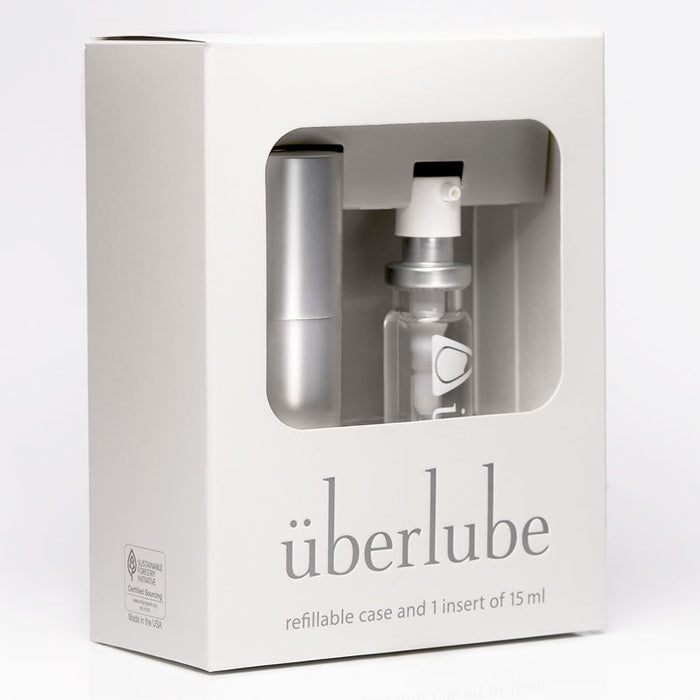 A white box for "überlube" displays a silver refillable case and a 15ml clear insert of lubricant through a cutout. The packaging indicates "refillable case and 1 insert of 15 ml" and is available at Worldcondoms.