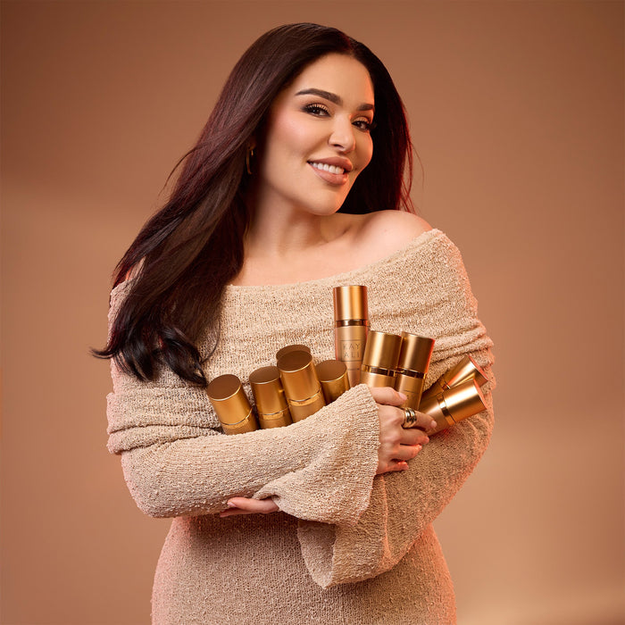 Mona Kattan holding gold cylindrical objects against a brown background