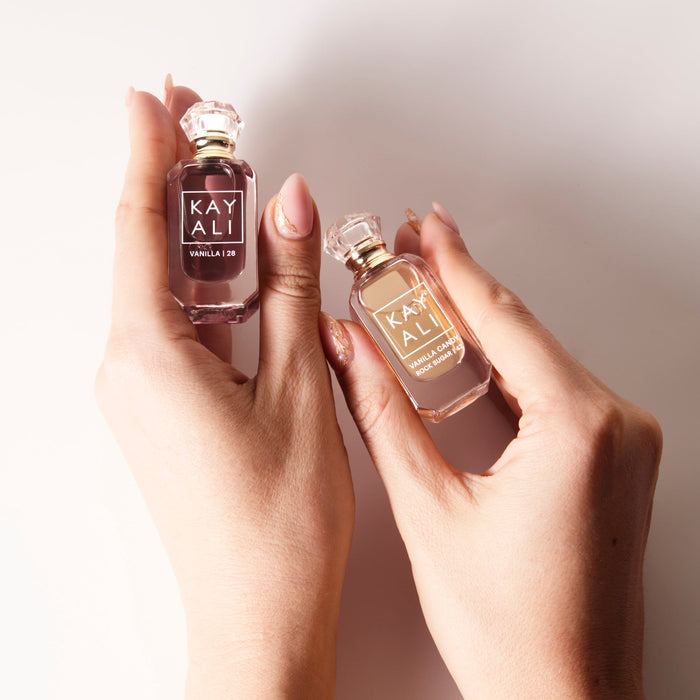 Two hands holding two small perfume bottles labeled 'KAYALI' against a neutral background.