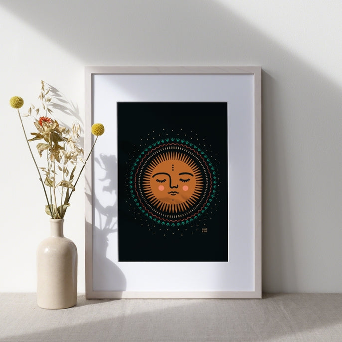 Framed Waking Up Sun Print 8x10 displayed on a table beside a vase of dried flowers.