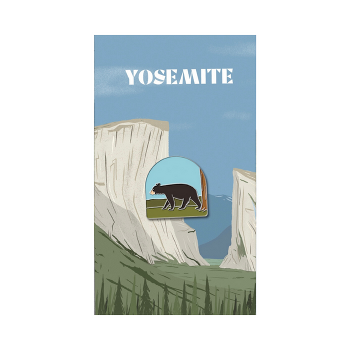 Enamel pin of a bear placed on a Yosemite National Park poster with canyon scenery.